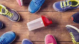 Auf einem Holzboden liegen mehrere Paare Laufschuhe, rings um eine Sport-Trinkflasche herum.