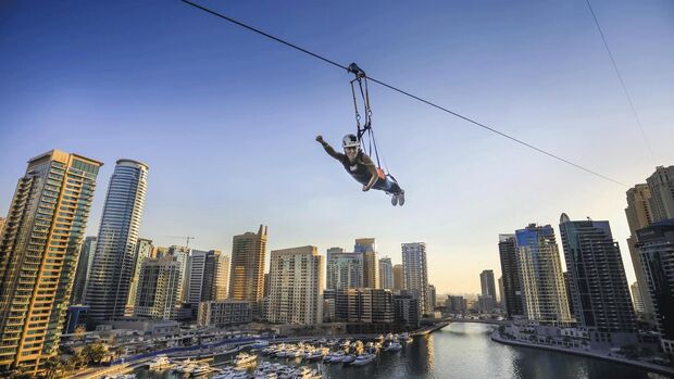 Ein Mann hängt an einer Zipline, die quer über den Hafen von Dubai gespannt ist