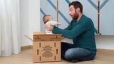 Ein Mann holt ein Neugeborenes aus einem Pappkarton