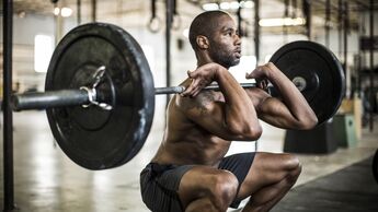 Ein Mann im Gym macht eine tiefe Kniebeuge mit einer schweren Langhantel.