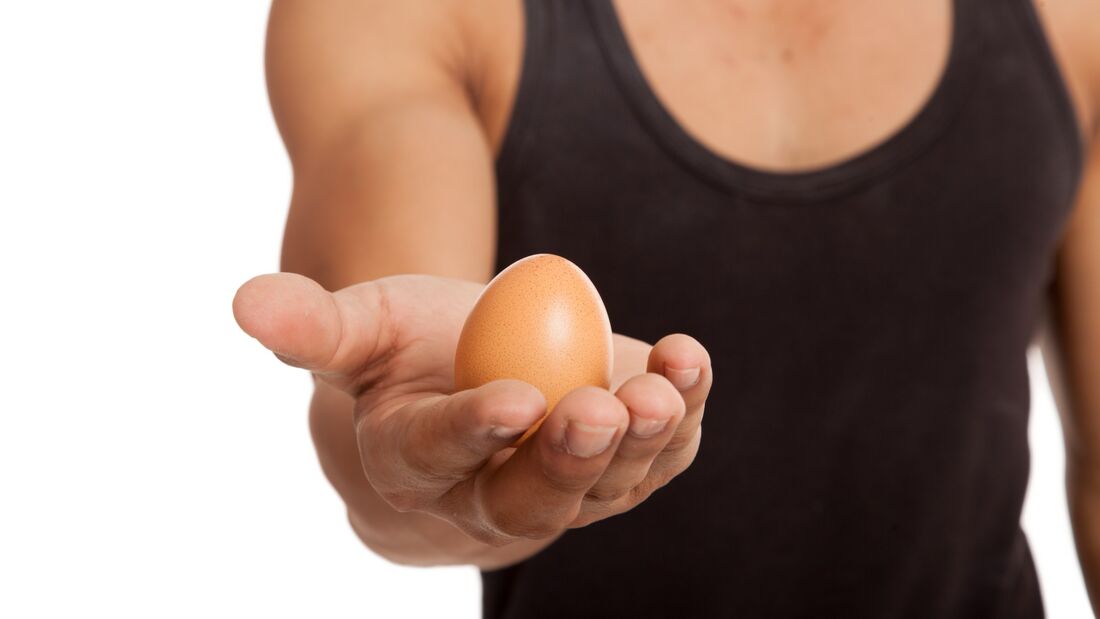 Ein Mann in einem schwarzen Tanktop hält ein Ei in die Kamera