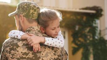 Ein Soldat in ukrainischer Militäruniform umarmt seine Tochter im Freien