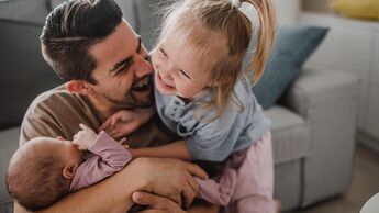 Ein Vater tobt mit seinen zwei kleinen Kindern vor dem Sofa