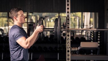 Ein junger sportlicher Mann baut im Gym eine Langhantel fürs Bankdrücken auf.