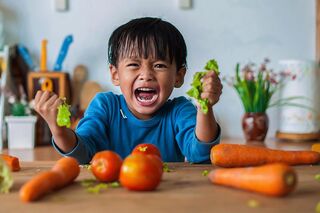 Ein wütendes Kind schreit in der Küche und zerfetzt Salatblätter