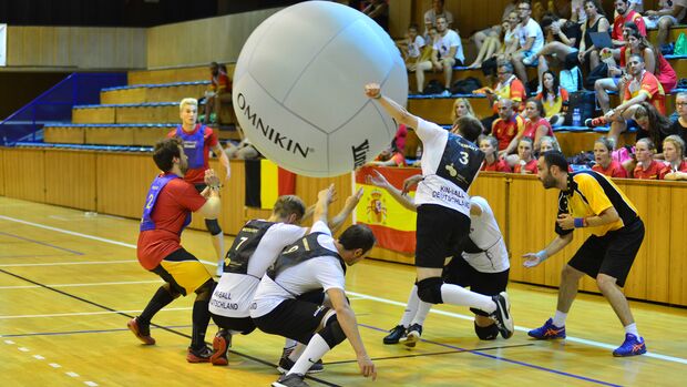 Eine Gruppe Männer spielt in einer Sporthalle mit einem großen Ball, der in die Luft geschlagen wird.