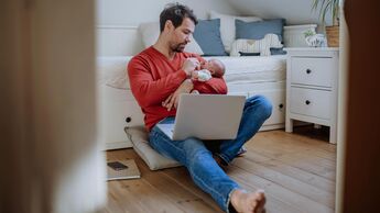 Frischgebackener Vater gibt seinem Nachwuchs das Fläschchen während er am Notebook sitzt