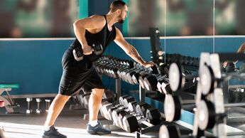 Kräftiger Mann greift zu Kurzhanteln im Gym.