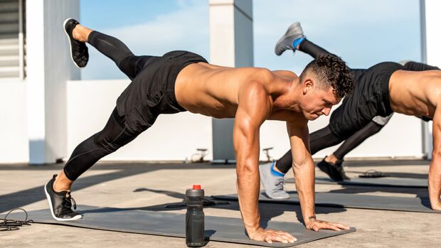 Männergruppe bei anstrengender Fitnessübung mit dem eigenen Körpergewicht im Stütz plus Beinheben.