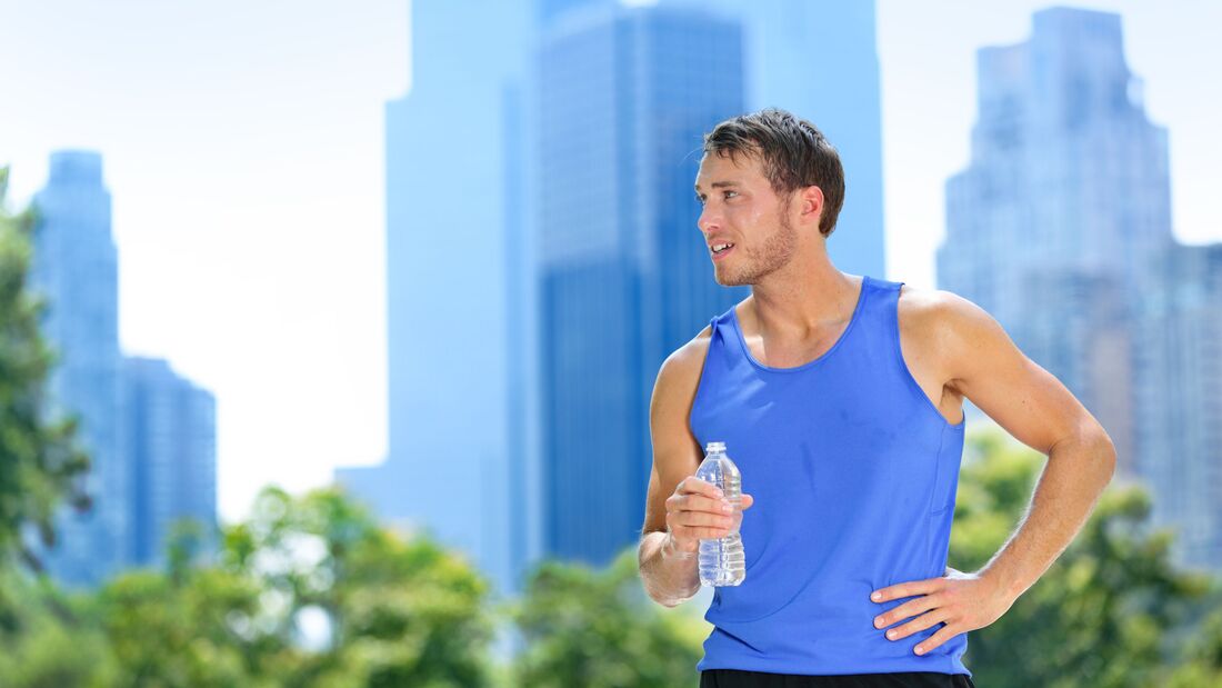 Männlicher Läufer steht schwitzend vor New Yorker Skyline mit einer Wasserflasche. 