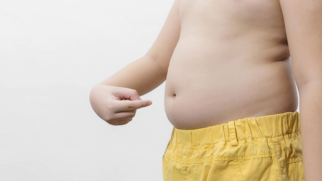 Man sieht den Oberkörper eines kleinen Jungen, der auf seinen Bauch zeigt.