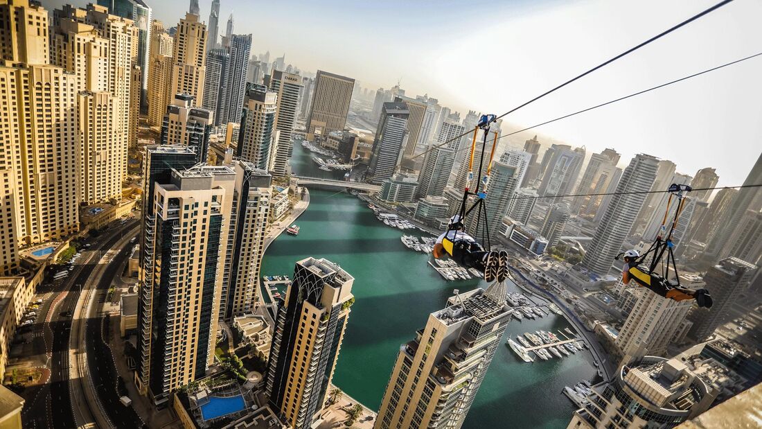 Man sieht eine Zipline über der Marina von Dubai an der eine Person hängt: Die Zipline ist über einen Kilometer langen und befindet 170 Meter über dem Erdboden