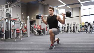 Mann bei einem Ausfallschritt mit einer Langhantel im Gym