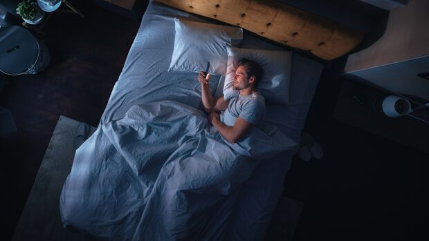 Mann liegt im Bett und spielt am Handy