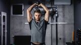Mann macht Trizepsüberzüge mit Hantel stehend im Gym.