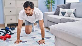 Mann macht im Wohnzimmer Fitnessübungen.