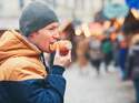 Mann mit Mütze isst auf dem Weihnachtsmarkt eine süße gefüllte Blätterteigrolle