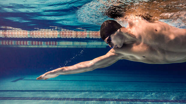 Mann mit schwarzer Badekappe schwimmt Kraul und wird unter Wasser fotografiert.