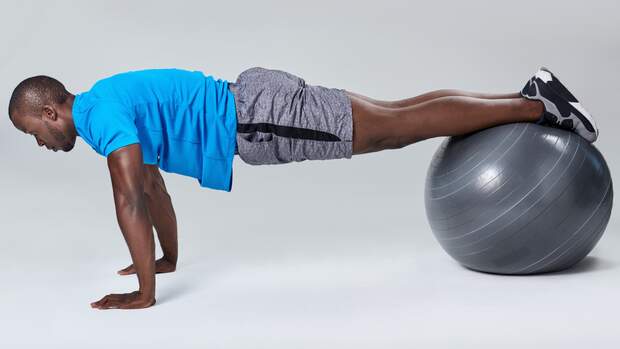 Mann stütz auf dem Boden mit den Füßen auf Gymnastikball
