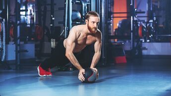 Mann trainiert im Fitnessstudio im Stütz auf einem Medizinball seinen Core.