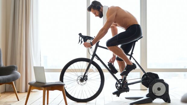 Muskulöser Mann radelt im Wohnzimmer auf seinem Rennrad in einer Rolle