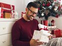 Smiling,Young,Man,Opening,Christmas,Gift,At,Home