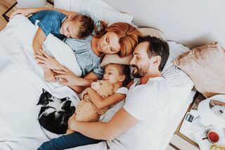 Vater, Mutter, zwei Kinder und eine Katze liegen alle zusammen in einem großen Bett und schlafen zufrieden