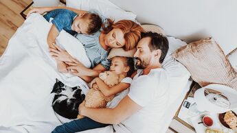 Vater, Mutter, zwei Kinder und eine Katze liegen alle zusammen in einem großen Bett und schlafen zufrieden