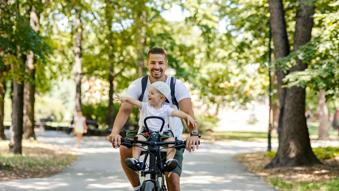 Vater fährt mit seinem Kind im Kindersitz Fahrrad
