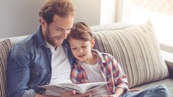 Vater hält seinen kleinen Sohn im Arm und liest ihm etwas vor. Beide schauen in ein Buch.