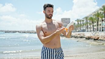 Young,Hispanic,Man,Tourist,Wearing,Swimsuit,Applying,Sunscreen,At,The