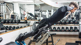 Young handsome fit man performing back-extension exercise on roman chair at gym.