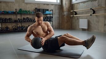 junger, durchtrainierter Mann trainiert seine definierten Bauchmuskeln mit einem Medizinball.