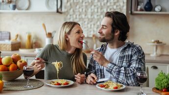 junges, lächelndes Paar isst gemeinsam ein Pasta-Gericht